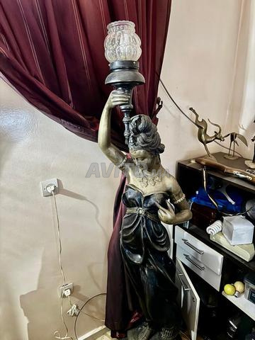 مصباح أرضي يصور امرأة ترتدي ملابس عتيقة، وذراعها اليمنى مرفوعة تحمل شعلة.